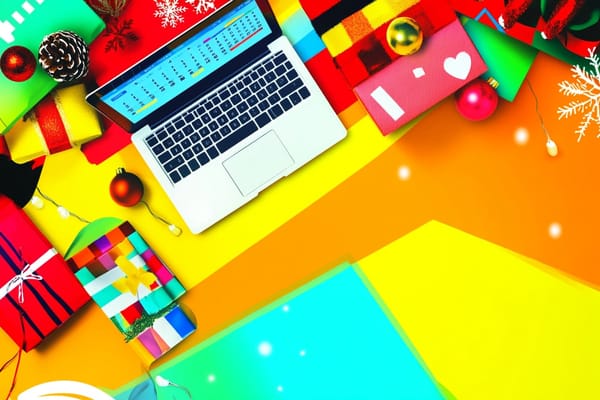 Top view of a desk with an open laptop and holiday gifts, ornaments, and wrapping paper